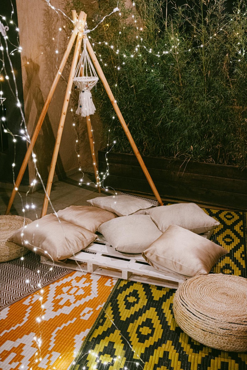 Floor cushions and woven poufs arranged on layered rugs with warm string lighting, showing the bohemian floor-seating aesthetic